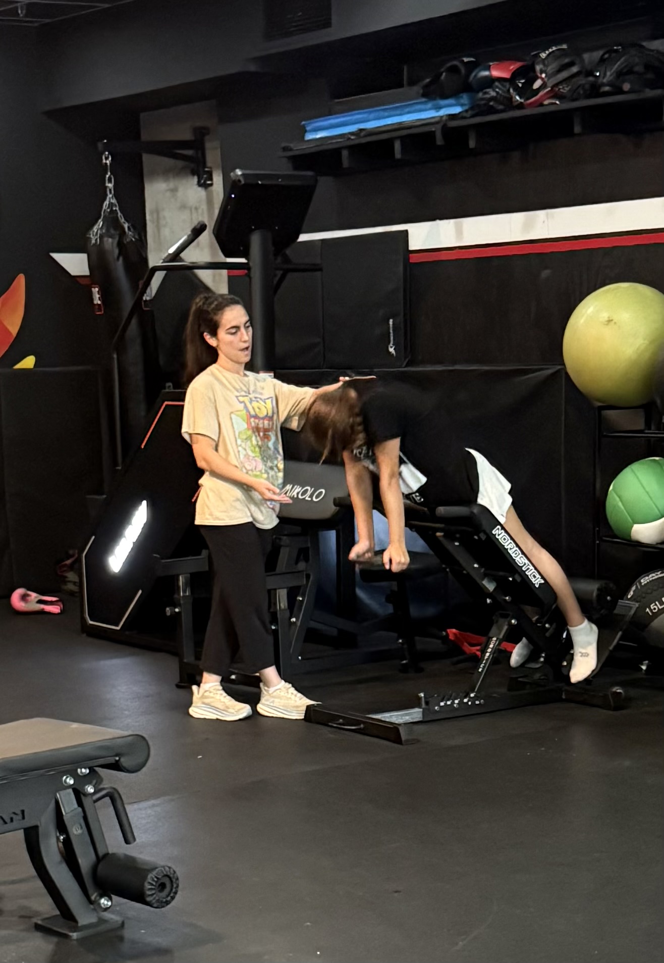 A trainer helping a member with form during a back extension exercise.