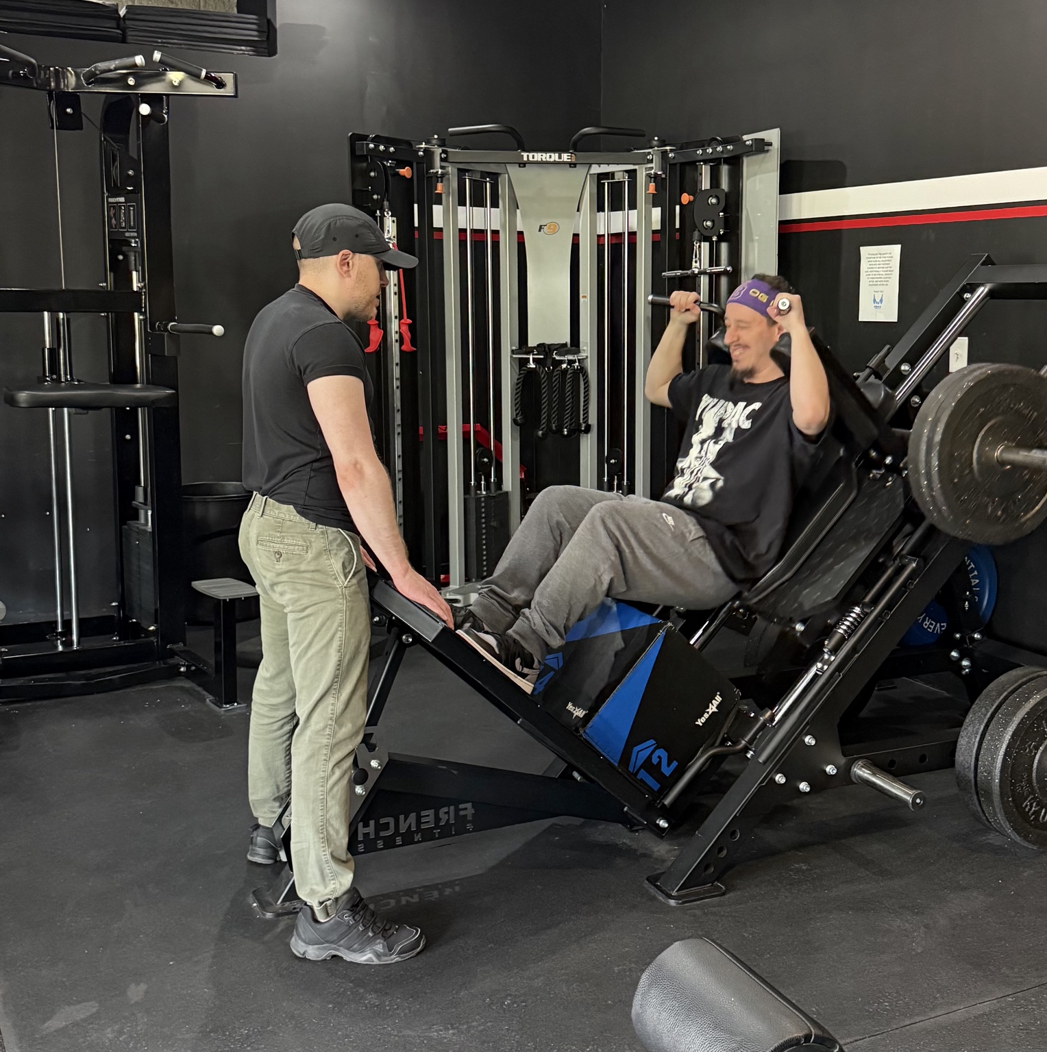 A trainer supporting a member during a leg press session.