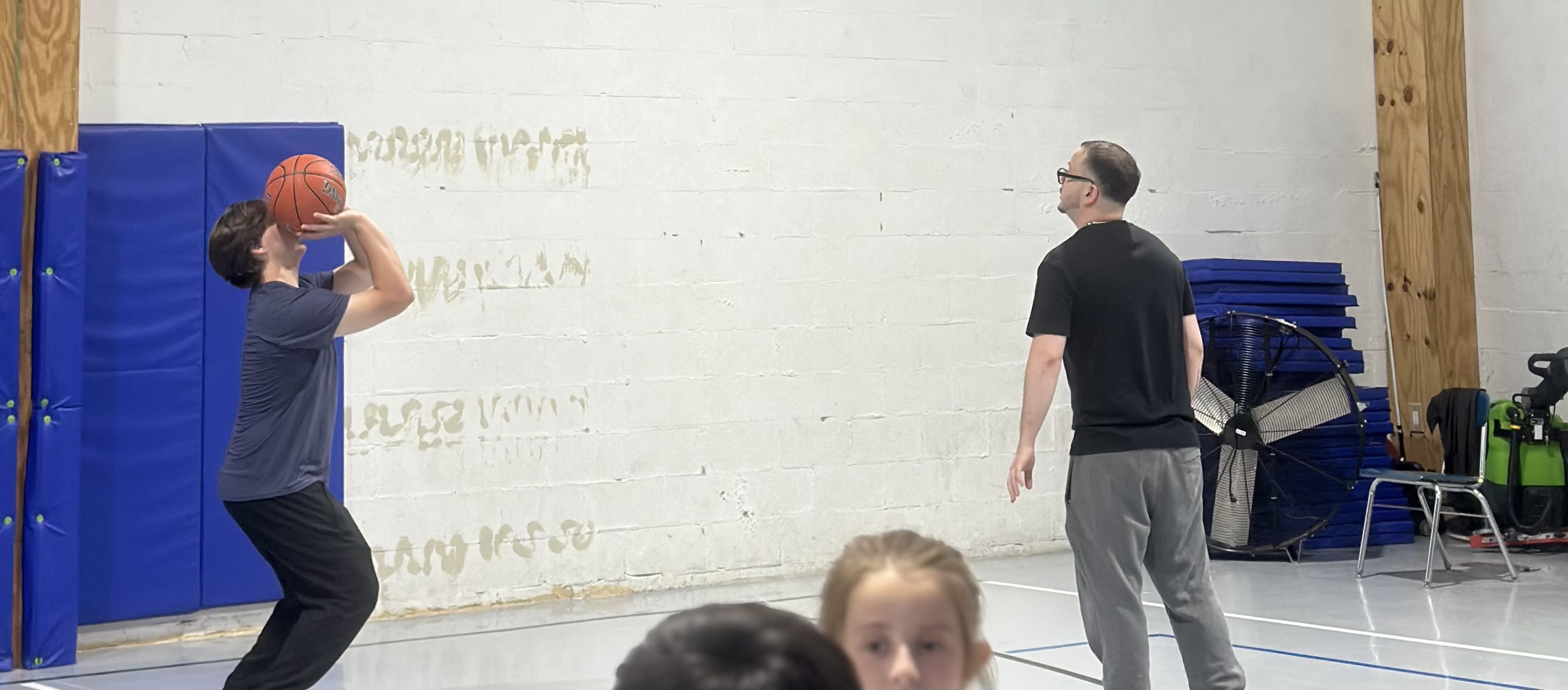 A basketball coach watching a player practice shooting technique.